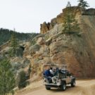silver jeep with passengers driving through mountain pass